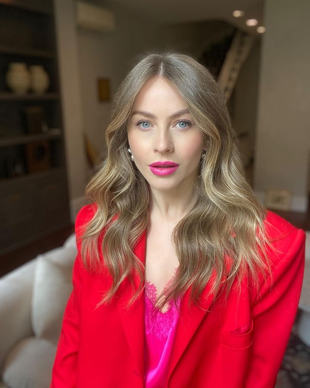 Julianne Hough in a red coat sitting on sofa.